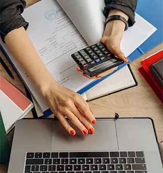 Femme tenant une calculatrice et travaillant devant son ordinateur