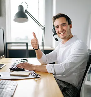 Homme avec un casque d'appel sur la tête, travaillant devant son ordinateur, souriant et lève son pouce